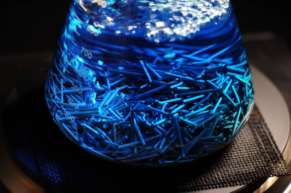 Metal specimens immersed in blue chemical indicator solution for intergranular corrosion testing.